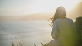 海辺で夕日を見つめる女性の後ろ姿。カウンセリングを受けた結果、心の変化を感じる瞬間。