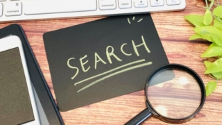 キーボード、スマートフォン、虫眼鏡と「SEARCH」と書かれた黒いカードが置かれた木製デスク