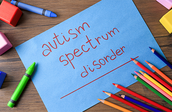 「autism spectrum disorder」と書かれた紙と周りに置かれた色鉛筆やブロック。自閉症スペクトラム障がい(ASD)の概念を表現するイメージ。