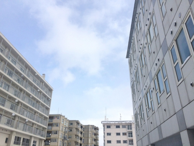 青空の下に建つ集合住宅の外観。複数のマンションやアパートが並んでいる。