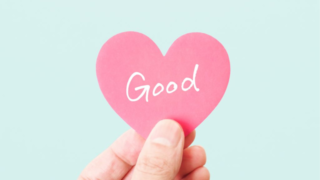 「Good」と書かれた赤いハート型の紙を手で持っているポジティブなイメージ。