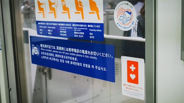 電車の優先席付近に貼られたヘルプマークと携帯電話マナーに関する案内表示。