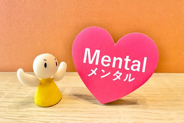 「Mental メンタル」と書かれたハートのオブジェと、黄色い服を着たキャラクターのイメージ。メンタルケアや心の健康をイメージ。
