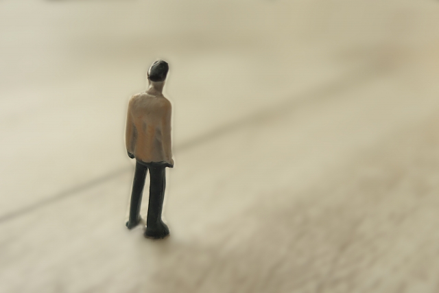 広い空間に一人で立つ小さな人形。孤独や障害受容、人生と向き合う覚悟を象徴するイメージ。