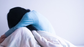 陰性症状による強い無気力で、ベッドの上でうつむき動けなくなっている様子