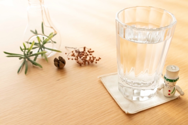 パニック障害の不調時に自宅でリラックスしながら水分補給をしている様子。コップの水とナチュラルな小物が置かれた落ち着いた空間。