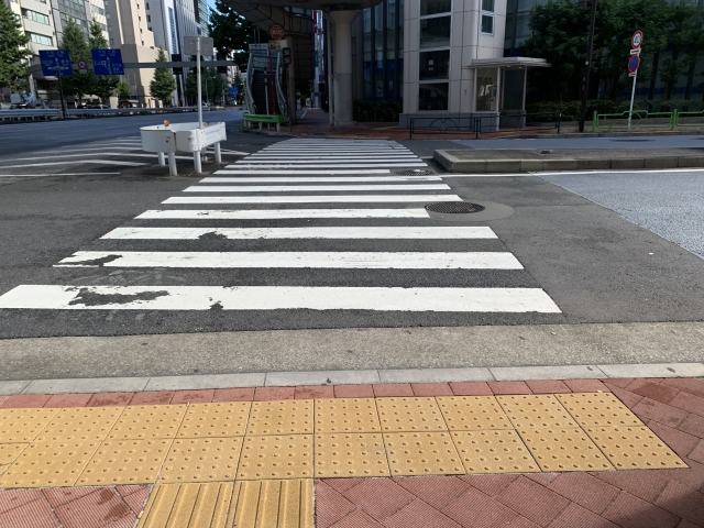 都市部の横断歩道手前に設置された点字ブロック。全盲者や視覚障害者の安全な道路横断を支えるバリアフリー設備の様子。
